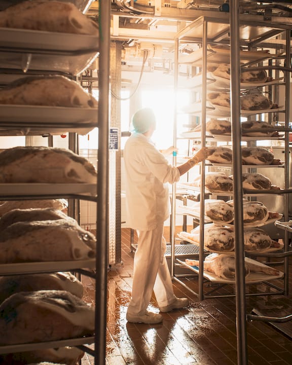 Addetto controlla teglie di prodotti da forno disposte su scaffalature all’interno di un laboratorio.