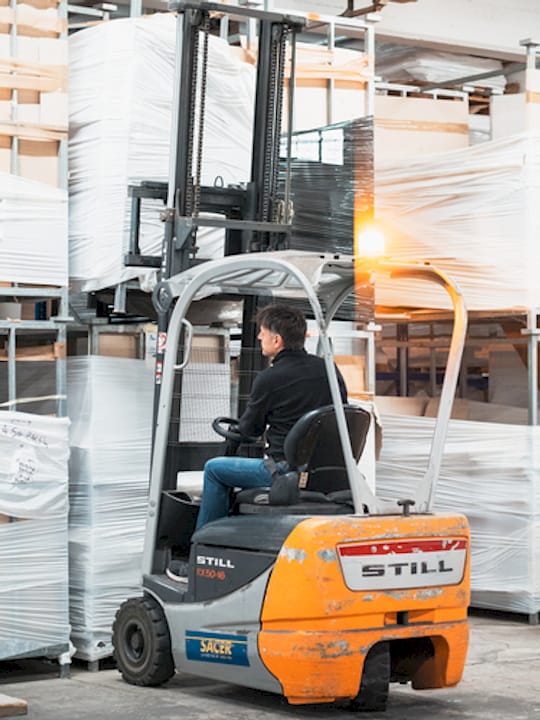 Operatore alla guida di un carrello elevatore movimenta pallet di materiali imballati all’interno di un magazzino industriale.