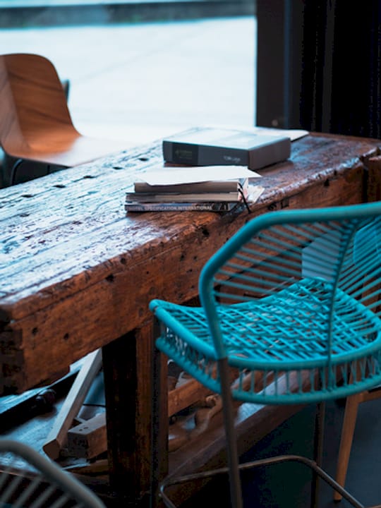 Tavolo in legno con libri e quaderni, circondato da sedie di design in un ambiente interno.